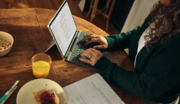 woman-typing-on-laptop-at-wooden-table-with-breakfast-.jpg Woman typing on laptop at wooden table with breakfast.