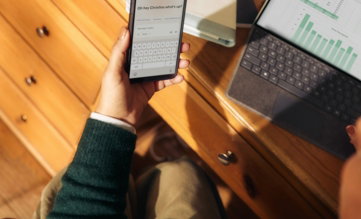 person-holding-phone-near-laptop-and-tablet-on-desk.jpg Person holding phone near laptop and tablet on desk